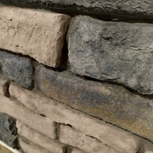A close-up view of a textured brick wall with both tan and dark gray stones, showing the rough, uneven surfaces and mortar lines—perfect inspiration for unique home siding.