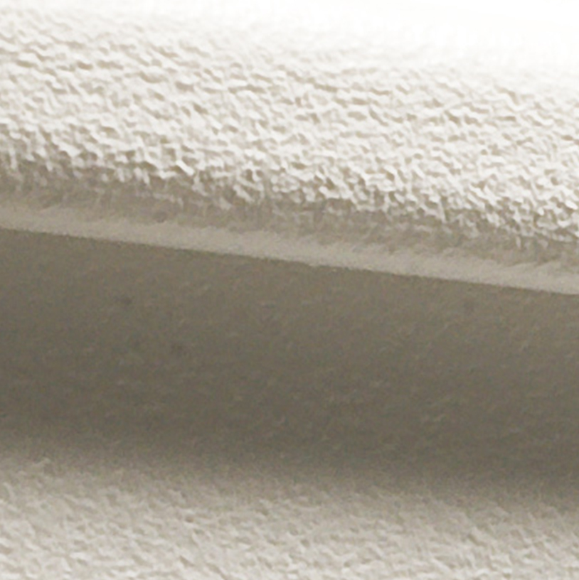 Close-up of a textured, off-white vinyl siding surface with a curved, raised edge casting a shadow. The image highlights the rough, grainy texture and subtle variations in light and shade.