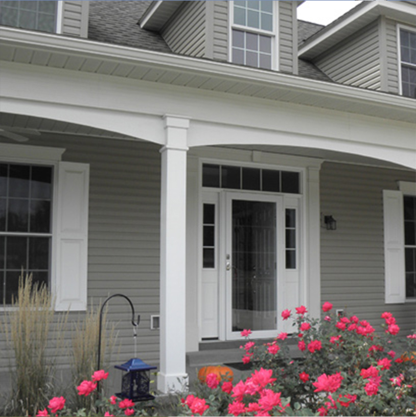Front porch of a house with gray vinyl siding, white trim, and a glass front door. Pink flowers and ornamental grasses line the walkway in front of the porch.